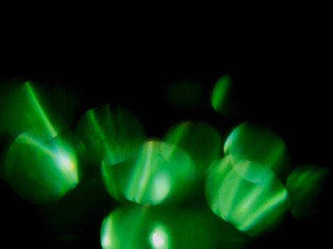 Green light bokeh against black background. Abstract glowing circles, dreamy and futuristic. Ideal for digital art, sci-fi themes, or tech backgrounds. Suggests mystery, energy, and modern vibes.