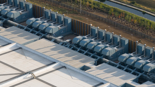 Aerial view of the Google Data Centre in Waltham Cross, featuring rows of industrial cooling units on the rooftop, adjacent to a canal and landscaped grounds in Cheshunt, England, United Kingdom.