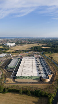 Aerial view of the Google Data Centre in Waltham Cross featuring a large modern industrial building with solar panels surrounded by green fields in Cheshunt, England, United Kingdom.