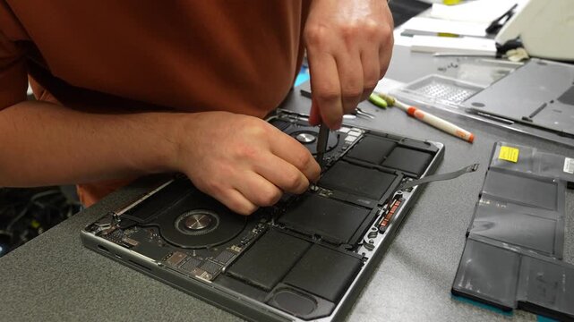 Technician opens laptop and examines internal components during repair on a workbench in an electronics service workshop