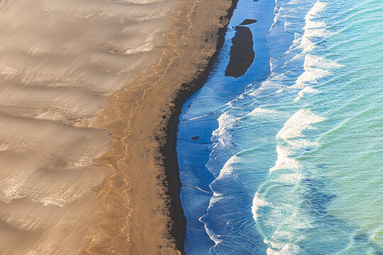 Aerial view of a black sand beach with turquoise waves crashing against the shore in Iceland.