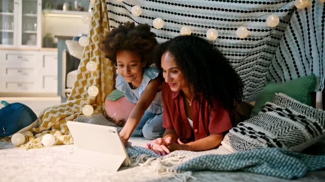 Mother daughter watching tablet cozy blanket fort. Happy family movie night.