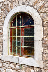 Obraz premium Arched window with iron grille set in weathered wooden frame within rough natural stone masonry wall in Patras, Greece.