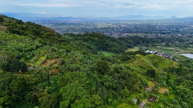 Aerial view of Bukit Sabak Sukabumi featuring lush green hills, dense tropical vegetation, terraced agricultural plots, and a distant valley landscape in Sukalarang, West Java, Indonesia.