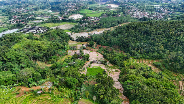 Aerial view of Bukit Sabak Sukabumi surrounded by lush green rice paddies, dense tropical forests, and small village houses in Sukalarang, West Java, Indonesia.