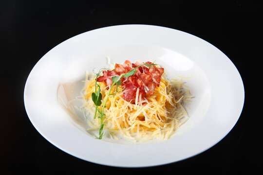 Italian pasta with crispy bacon and grated cheese. White plate, black background. Garnished with fresh herbs