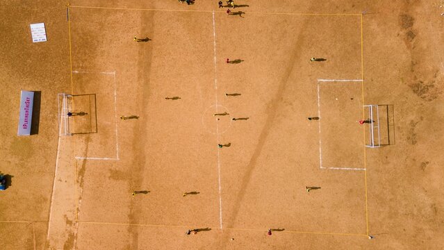 Aerial view of a soccer match played on a dry dirt field with players moving across the pitch and goalposts visible in Matheran, Maharashtra, India.
