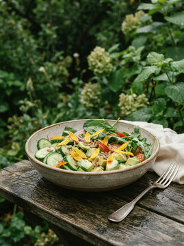 Ceramic bowl of salad with avocado on a weathered table in a lush garden