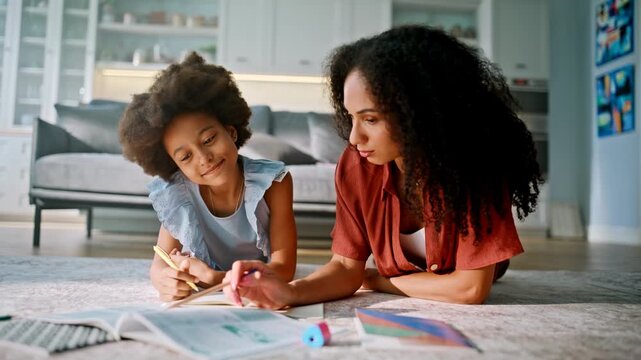 Mother helping child homework living room floor. Multiracial family learning.