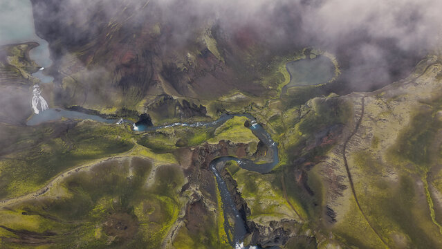 Aerial view of the Raudibotn crater area featuring a winding river, vibrant mossy volcanic terrain, and low-hanging clouds in Svartafellstangi, Skaftarhreppur, Iceland.