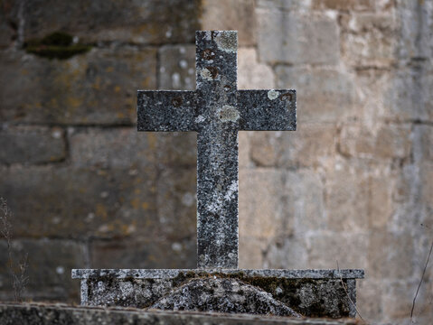 Detail view of a stone cross on a pedestal of the same material but deteriorated by the passage of time on top of a tomb in the door of a church