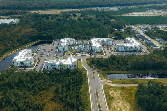 Aerial view of a modern residential apartment complex surrounded by dense forest, parking lots, and small ponds in Jacksonville, Florida, United States.