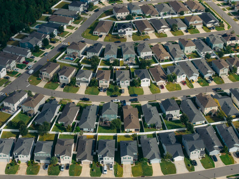 Aerial view of a suburban housing development featuring rows of identical residential houses with green lawns and white fences in a planned community in Jacksonville, Florida, United States.