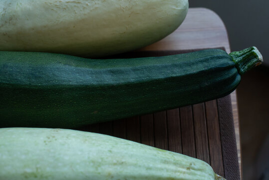 Three zucchinis of varying colors and sizes are arranged on a wooden cutting board. The scene emphasizes fresh vegetables and healthy eating.