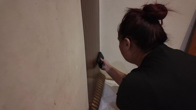Person applies wallpaper along wall trim with care and precision
