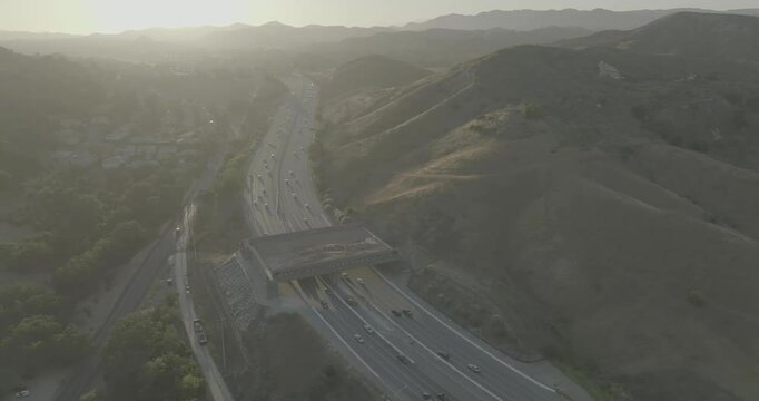 Drone shot over busy highway and overpass in backlit hazy hills