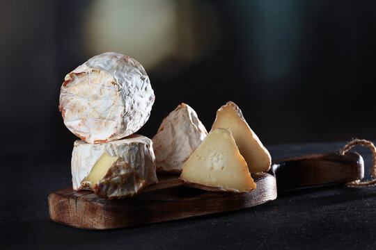 Cut brie cheese on wooden board. Soft creamy texture, white mold rind. Dark background. Gourmet food photography. Copy space