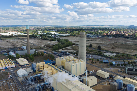 Aerial view of an industrial power plant with tall chimneys, storage tanks, and surrounding buildings in the United Kingdom.