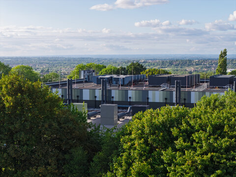 Aerial view of a data center featuring rooftop cooling units and industrial infrastructure, surrounded by lush green trees with a distant landscape in the United Kingdom.