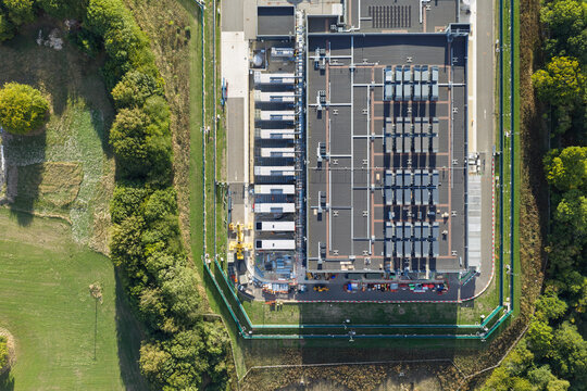 Aerial view of a modern data center facility featuring rooftop cooling units and technical infrastructure, surrounded by green fields and trees in the United Kingdom.