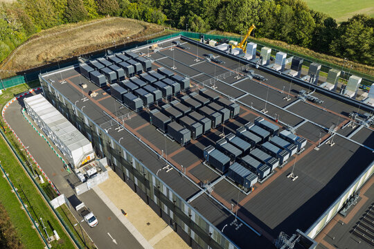 Aerial view of a modern data center rooftop featuring rows of cooling units and technical infrastructure surrounded by green trees in the United Kingdom.