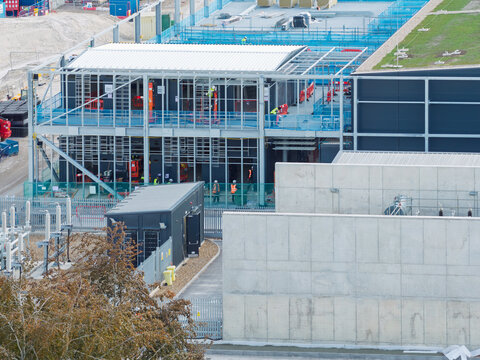 Aerial view of a data center construction site featuring a steel framework, workers in high-visibility gear, concrete walls, and a green roof section in the United Kingdom.