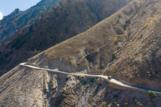 Aerial view of the dangerous Fairy Meadows Road winding along steep mountain slopes with a jeep driving on the narrow dirt path in Fairy Meadows, Gilgit-Baltistan, Pakistan.