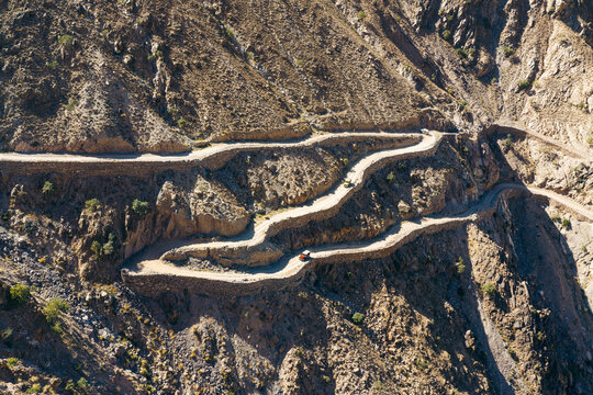 Aerial view of the winding and dangerous Fairy Meadows Road carved into steep rocky mountain slopes with a jeep driving along the narrow path in Fairy Meadows, Balochistan, Pakistan.