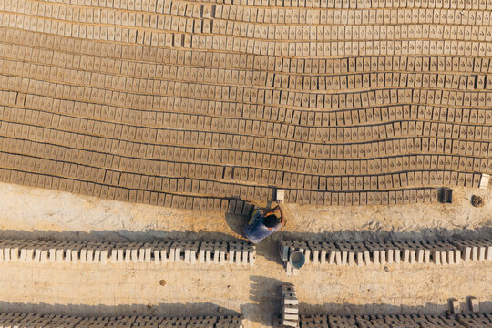 Aerial view of a worker arranging rows of sun-dried clay bricks at a traditional brick factory in Lahore, Punjab, Pakistan.
