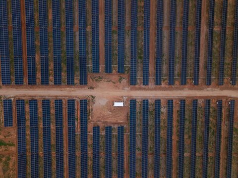 Aerial view of rows of solar panels in a large photovoltaic power plant with a central maintenance area and dirt access roads in Bonnievale, Western Cape, South Africa.
