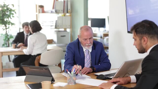 Elderly bank employee discusses financial matters with a young man at the table. Senior bank employee offers the client to open a deposit and a savings account . High quality 4k footage