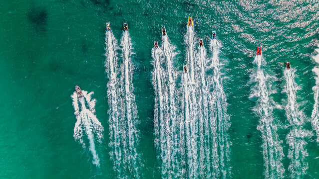Aerial view of multiple motorboats speeding across the turquoise waters of Gordon's Bay, leaving long white wakes behind them in Cape Town, Western Cape, South Africa.