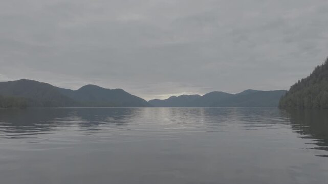 Calm fjord reflecting overcast sky with low mountain silhouettes