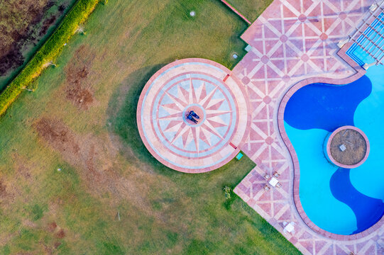 Aerial view of an elegant resort with a swimming pool and circular deck featuring traditional Rajasthani stonework, with two people on the geometric pattern in Jodhpur, Rajasthan, India.