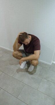 Man kneels with his head lowered and a hand on his head, portraying worry, sadness and emotional strain