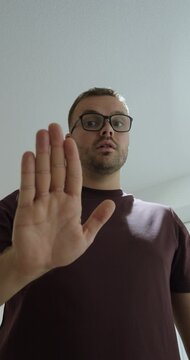 Man wearing glasses raises an open palm toward the camera in a stop gesture, representing boundaries, refusal and clear communication