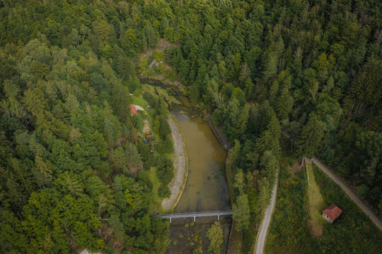 Aerial view of Zapora Zlotnicka dam surrounded by dense forest, a small bridge over the river, and a winding road in Zlotniki Lubanskie, Lower Silesian Voivod, Poland.