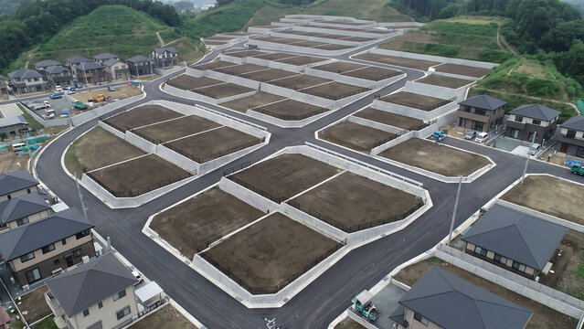 ドローンで見下ろした丘陵地の道路に沿ってコンクリート擁壁で区切られた分譲区画が並ぶ造成地