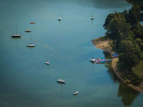 Aerial view of sailboats moored on the calm waters of the lake near Czocha Castle, surrounded by lush green trees and a small pier in Sucha, Wojewodztwo dolnoslaskie, Poland.