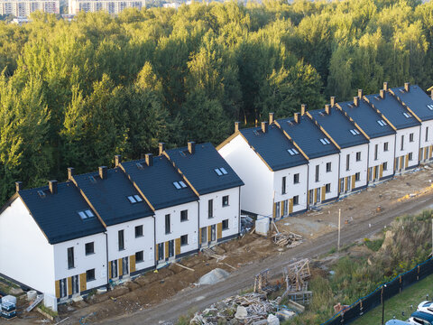 Aerial view of a row of modern white houses with dark roofs under construction, surrounded by lush green trees in Wieliczka, Lesser Poland Voivode, Poland.