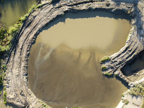 Aerial view of a muddy circular reservoir with sediment patterns and disturbed earth banks in Niedzica, Lesser Poland Voivode, Poland.