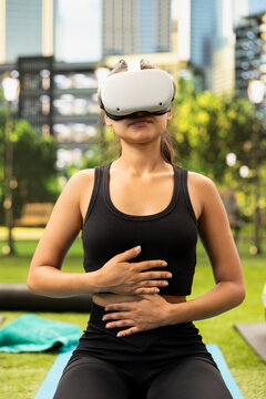 Woman wearing virtual reality glasses with hands on abdomen during guided controlled breathing and mindfulness exercise in urban park.