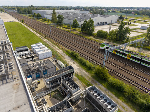 Aerial view of an AI data center with industrial cooling units on the roof, situated next to railway tracks with a passing train in Krakow, Lesser Poland Voivode, Poland.