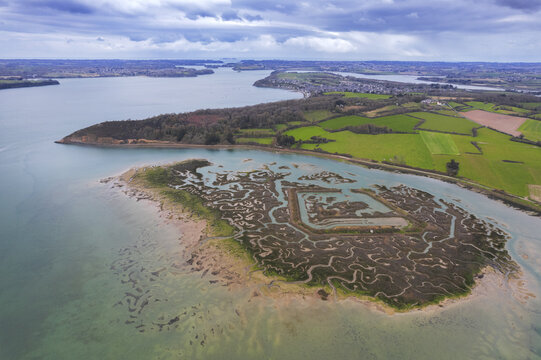 Aerial view of the Rance river estuary with its intricate tidal flats and marshy islands surrounded by lush green fields near Saint-Suliac, Brittany, France.
