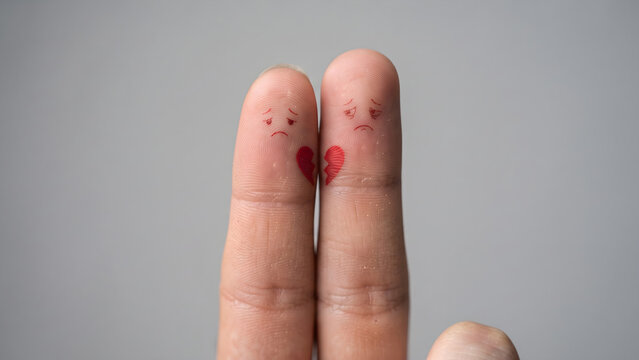 Two Fingers Painted with Sad Faces and Broken Heart Symbols Representing Emotional Pain and Relationship Breakup Concepts