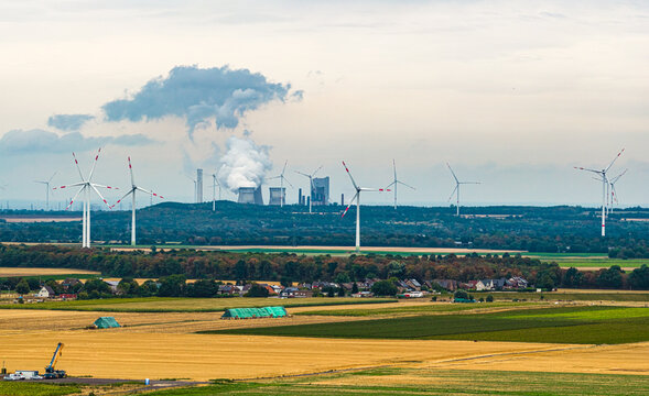 Aerial view of Tagebau Hambach with wind turbines, agricultural fields, and a power plant emitting steam in the distance in Elsdorf, Nordrhein-Westfalen, Germany.