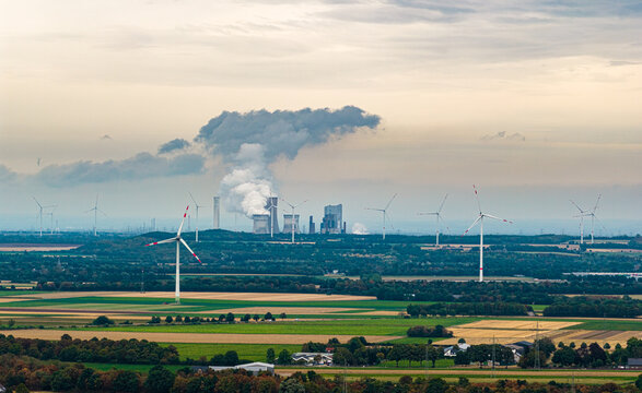 Aerial view of Tagebau Hambach with wind turbines and agricultural fields in the foreground, and a power plant emitting steam in the distance, Elsdorf, Nordrhein-Westfalen, Germany.