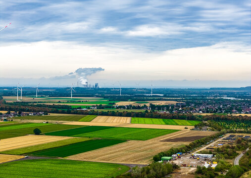 Aerial view of Tagebau Hambach open-pit mine with wind turbines, agricultural fields, and industrial power plant in the distance under a cloudy sky in Elsdorf, Nordrhein-Westfalen, Germany.