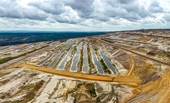 Aerial view of the Tagebau Hambach open-pit mine featuring rows of solar panels installed within the vast industrial landscape under a cloudy sky in Elsdorf, Nordrhein-Westfalen, Germany.