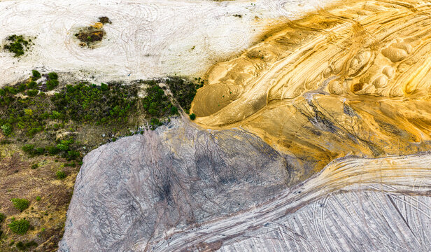 Aerial view of Tagebau Hambach open-pit mine showing contrasting textures of yellow sand, grey soil, and green vegetation with tire tracks in Elsdorf, Nordrhein-Westfalen, Germany.